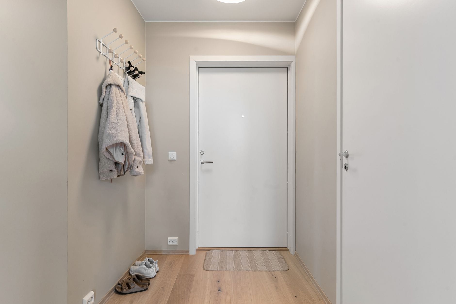 Minimalistyczne wejście do mieszkania z drewnianą podłogą i wieszakami