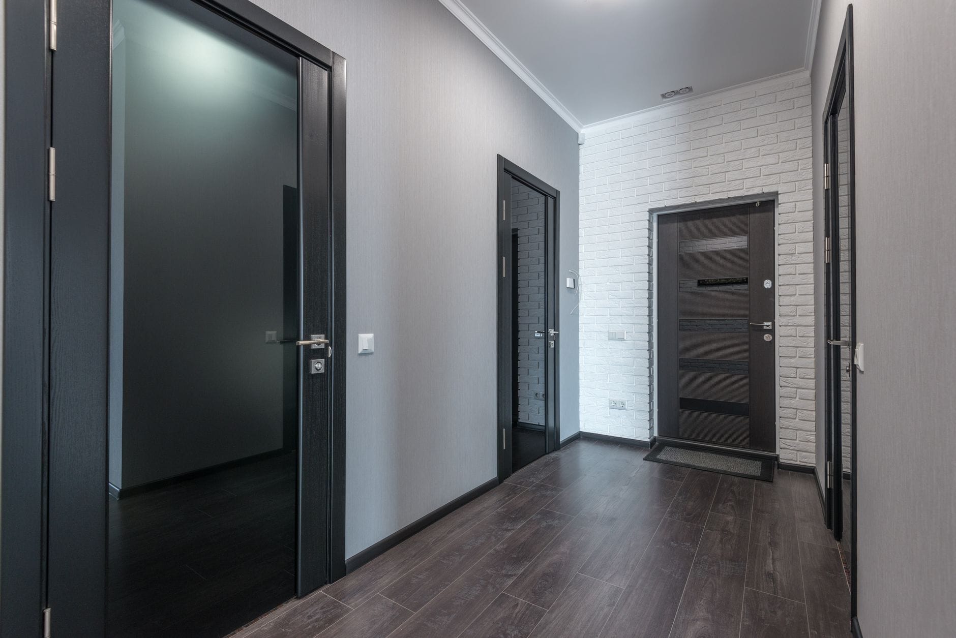 Szary korytarz z laminatem i czarnymi drzwiami z przeszkleniami